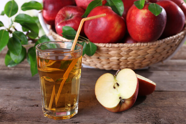 Glass of apple juice with red apples on wooden table, closeup