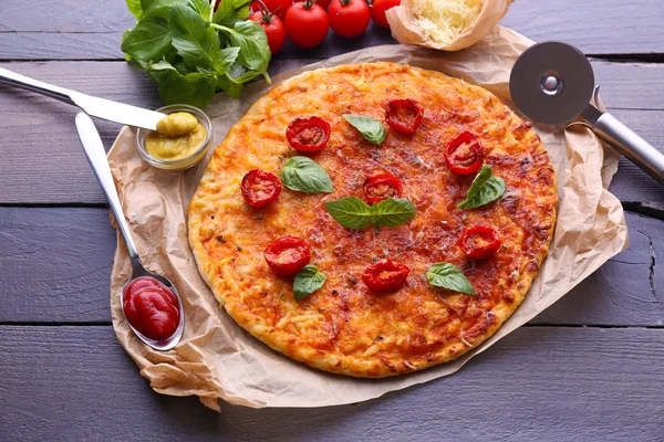 Pizza z bazylią i pomidorkami na pergamin na drewnianym stole tło — Zdjęcie stockowe
