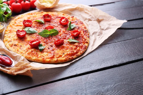 Pizza with basil and cherry tomatoes on parchment on wooden table background — Stock Photo, Image