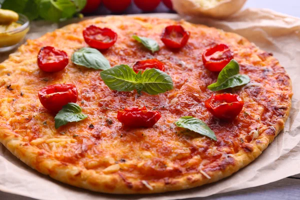 Pizza con basilico e pomodorini su pergamena su tavola di legno, primo piano — Foto Stock