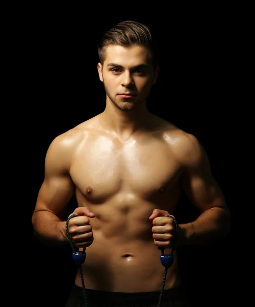 Muscle young man exercising with resistance band on dark background — Stock Photo, Image