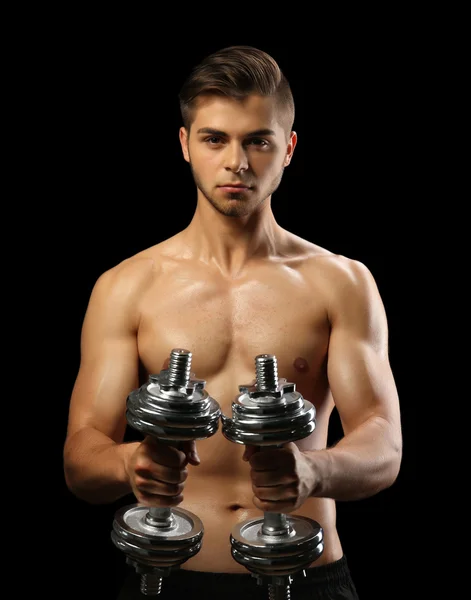 Muscle young man holding dumbbells on dark background — Stock Photo, Image