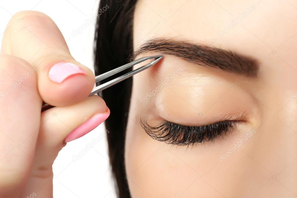 Young woman plucking eyebrows with tweezers close up