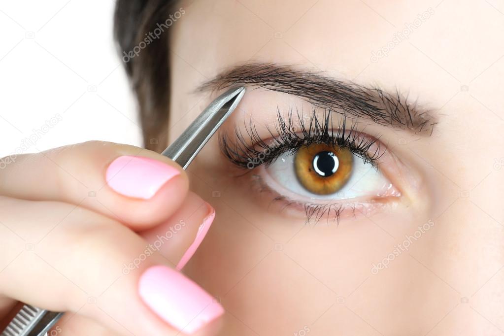 Young woman plucking eyebrows with tweezers close up