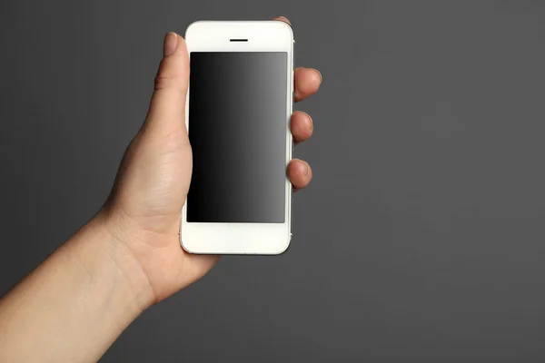 Mão segurando telefone inteligente móvel no fundo cinza — Fotografia de Stock