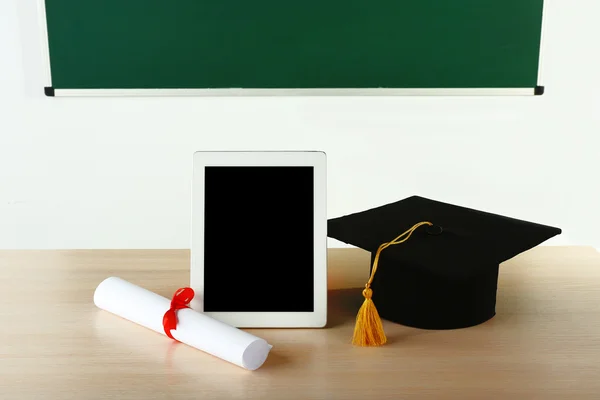 Tapa de graduación con tableta y diploma en la mesa en clase — Foto de Stock
