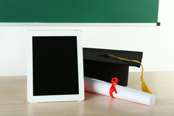 Capa de graduação com tablet e diploma na mesa em classe — Fotografia de Stock