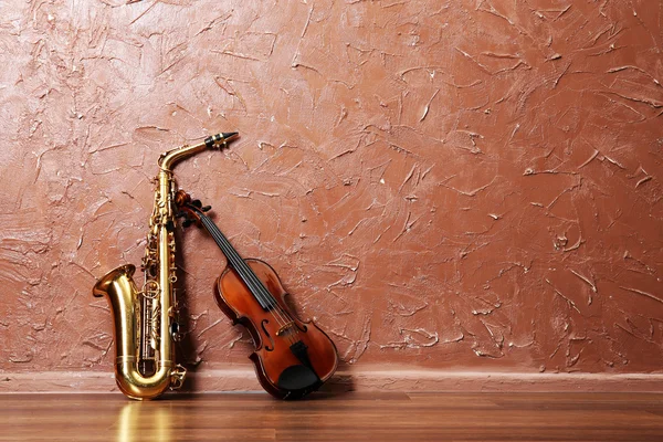 Saxofon und Geige auf braunem Wandhintergrund — Stockfoto