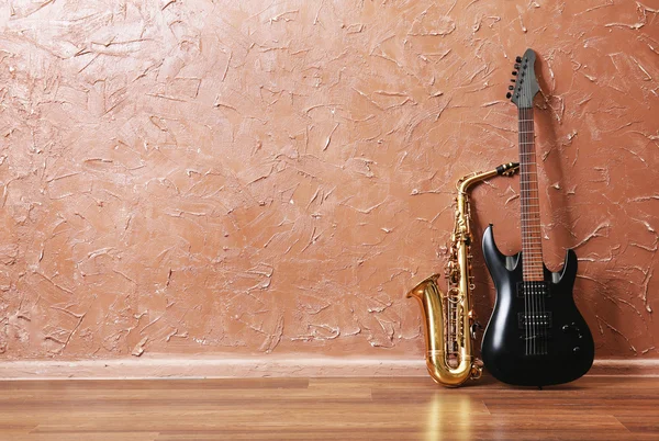 Электрогитара и саксофон на фоне коричневой стены — стоковое фото