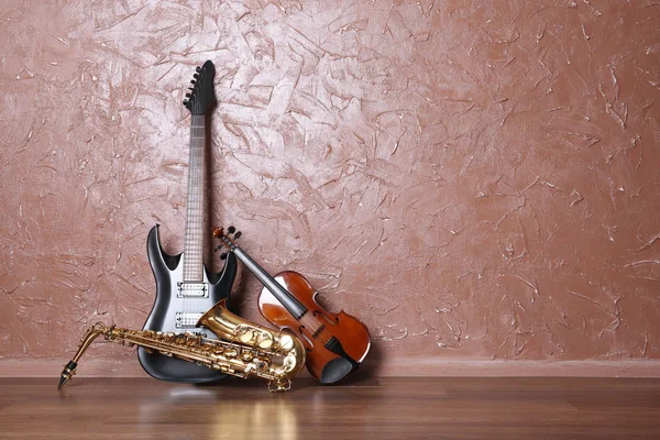 Guitarra elétrica, saxofone e violino no fundo da parede marrom — Fotografia de Stock