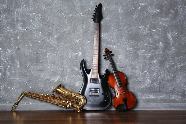 Guitarra eléctrica, saxofón y violín sobre fondo de pared gris —  Fotos de Stock