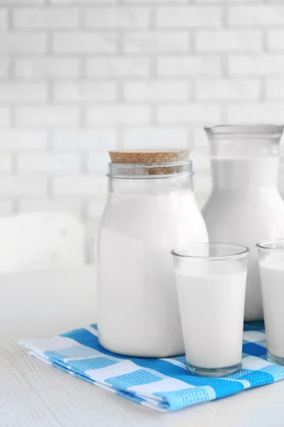 Werper, kruik en glas melk op houten tafel, op bakstenen muur achtergrond — Stockfoto