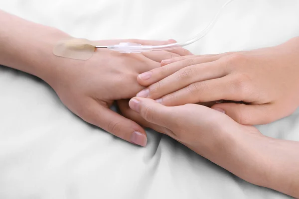 Frauenhände halten geduldige Hand mit Dropper-Nadel auf dem Bett in Großaufnahme — Stockfoto