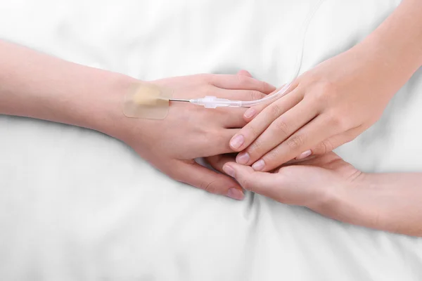 Mãos femininas segurando a mão do paciente com agulha conta-gotas na cama close-up — Fotografia de Stock