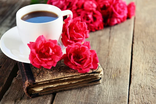 Old book with beautiful roses and cup of coffee on wooden table close up — Stock Photo, Image
