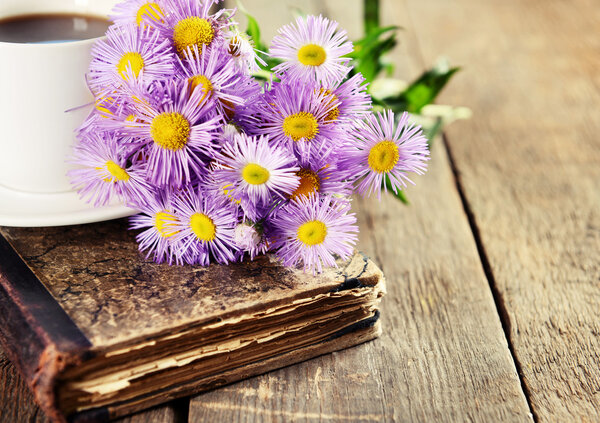 Старая книга с красивыми цветами и чашкой чая на деревянном столе крупным планом
