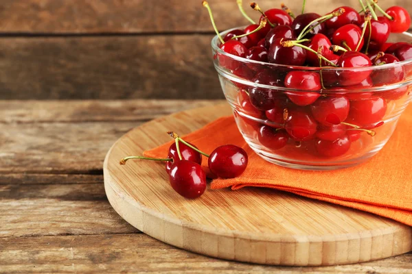 Cerises fraîches dans un bol en verre avec serviette sur fond en bois — Photo