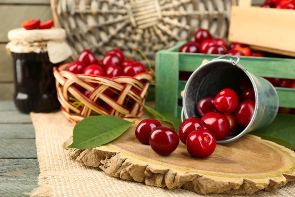 Cerises douces avec feuilles vertes dans un seau et des boîtes en bois, sur fond en bois — Photo