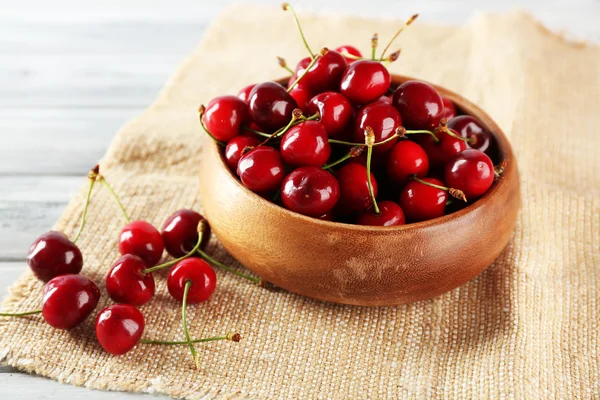 Fresh cherries in bowl with sackcloth on wooden table, closeup — Stock Photo, Image