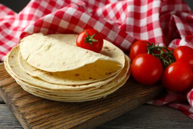 Ev yapımı kepekli un tortilla ve ahşap masa arka plan üzerinde kesme tahtası üzerinde sebze yığını