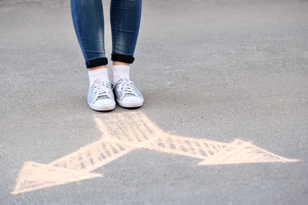 Pieds féminins et flèches de dessin sur fond de chaussée — Photo