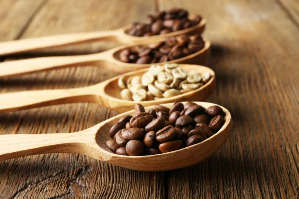 Grãos de café em colheres no fundo de madeira — Fotografia de Stock