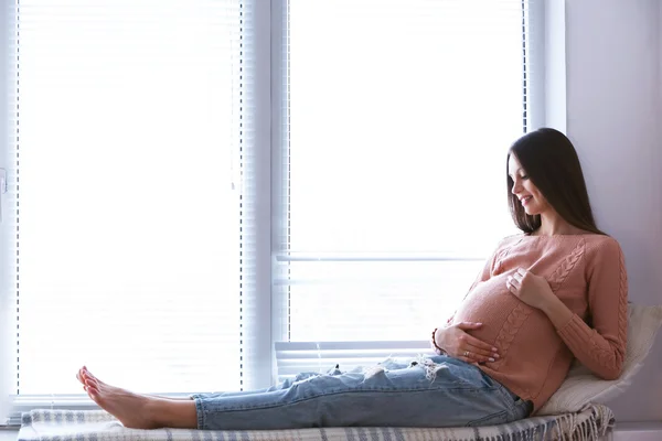 Wanita hamil yang duduk di latar belakang jendela — Stok Foto