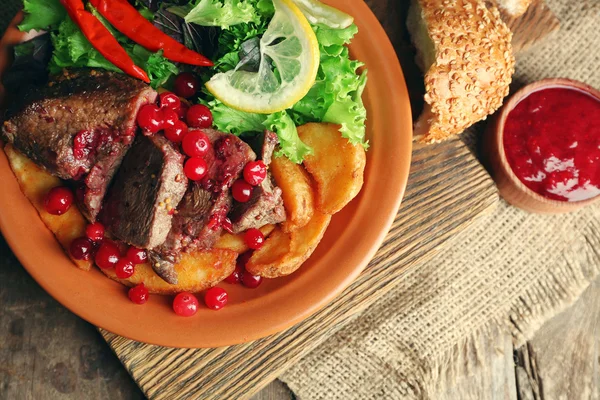 Sabrosa carne asada con salsa de arándanos, ensalada y verduras asadas en el plato, sobre fondo de madera — Foto de Stock