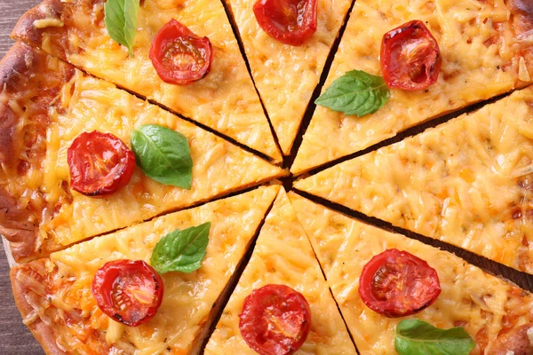 Segmenten van smakelijke kaas pizza met basilicum en cherry tomaten op tafel close-up — Stockfoto