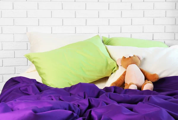 Lit confortable avec oreillers et ours en peluche dans la chambre — Photo