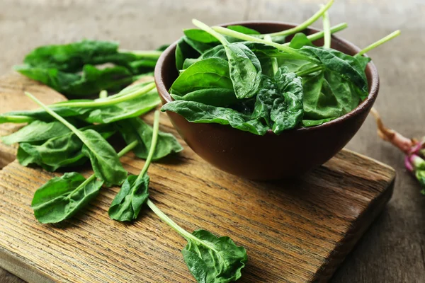 Bowl of fresh spinach leaves on wooden cutting board, closeup — Stock Photo, Image