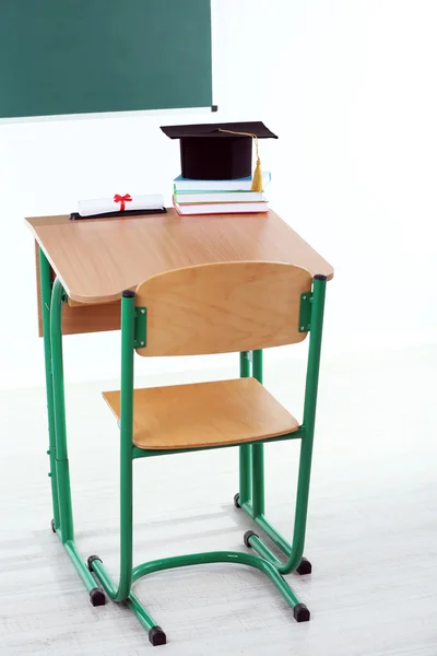 School desk with master hat, stack of books and diploma in classroom — Stock Photo, Image