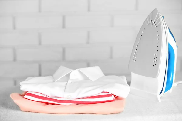 Pile of clothes and electric iron on brick wall background — Stock Image Pile of clothes and electric iron on brick wall background Stock Picture