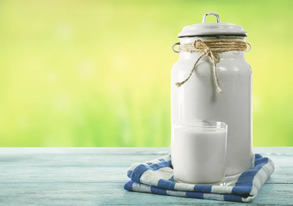 Retro can for milk and glass of milk on wooden table, on green background — ストック写真