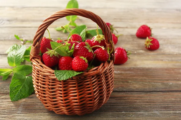 Ripe strawberries in wicker basket on wooden table, closeup — Stock Photo, Image