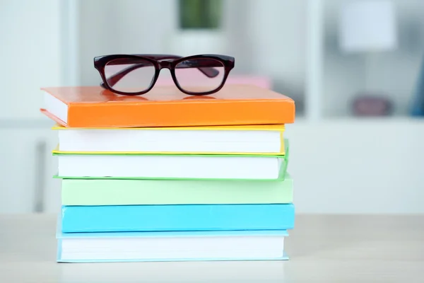 Stack of books with glasses on wooden table in room — Stock Photo, Image