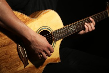 Genç adam akustik gitarla karanlık arka planda çalıyor.