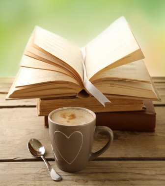 Cup of coffee and books on wooden table, on green background