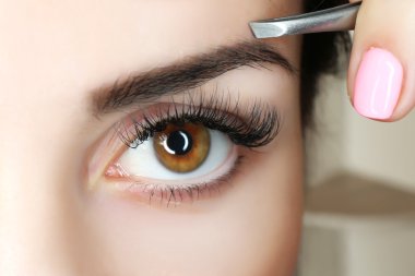 Young woman plucking eyebrows with tweezers close up clipart