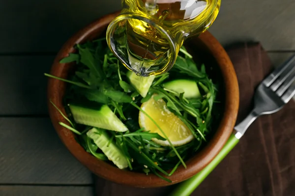 Poring salada verde com azeite sobre mesa de madeira, close-up — Fotografia de Stock