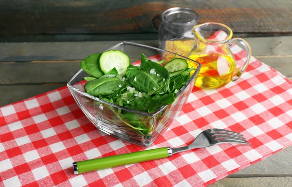 Cuenco de vidrio de ensalada verde con pepino y espinacas en mesa de madera con servilleta, primer plano —  Fotos de Stock