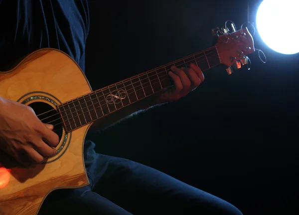 Genç adam akustik gitarla karanlık arka planda çalıyor. — Stok fotoğraf