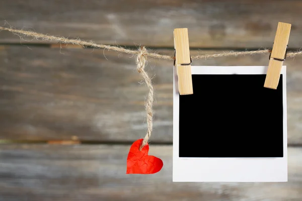 Corazón brillante y papel fotográfico colgando de una cuerda sobre fondo de madera — Foto de Stock