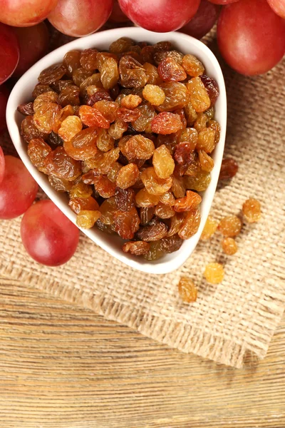 Raisins in bowl with grapes on table close up — Stock Photo, Image