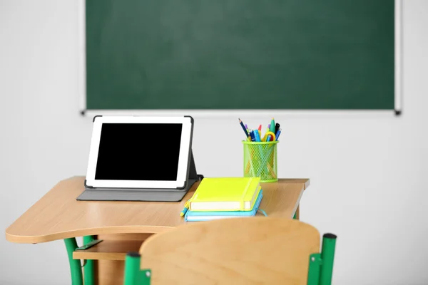 Escritorio de madera con papelería y tableta en clase sobre fondo pizarra —  Fotos de Stock