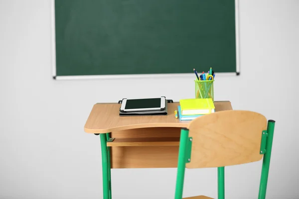 Wooden desk with stationery and tablet in class on blackboard background — Stock Photo, Image