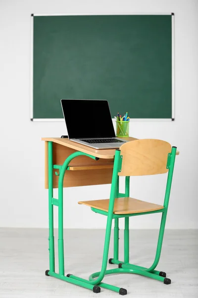 Wooden desk with stationery and laptop in class on blackboard background — Stock Photo, Image