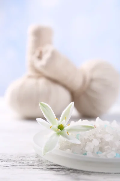 Sea salt, flowers and spa treatment on color wooden table, on light background — Stock Photo, Image