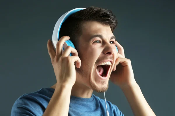 Bonito jovem ouvindo música em fundo cinza — Fotografia de Stock