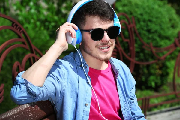 Homem com fones de ouvido descansando no banco no parque — Fotografia de Stock